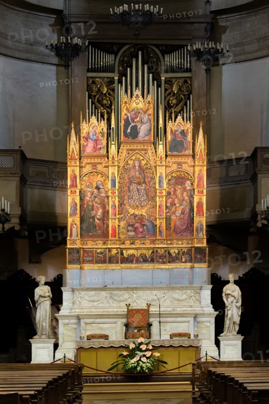 Montepulciano, Duomo (Cathedral of S. Maria Assunta), the interior, the main altar: the monumental "Triptych of the Assumption", painted by Taddeo di Bartolo in 1401. The central panel of the triptych shows the monumental figure of the Madonna Assunta surrounded by Angels, while below are visible the twelve apostles crowding around the empty tomb of the Madonna. Above the Assumption we see the Coronation of the Virgin. The three scenes must be read as a time sequence from bottom to top with the Death of the Virgin, her Assumption and her Coronation. The two side panels depict various Saints in the attitude of adoring the central figure of the Madonna, while on the four pillars that delimit the various panels we see twelve small figures of Doctors of the Church (three per pillar). Above the two side panels are the Announcing Angel (on the left) and the Madonna Annunziata (on the right). The predella at the bottom depicts Nine scenes from the life of Jesus Christ while above the predella...