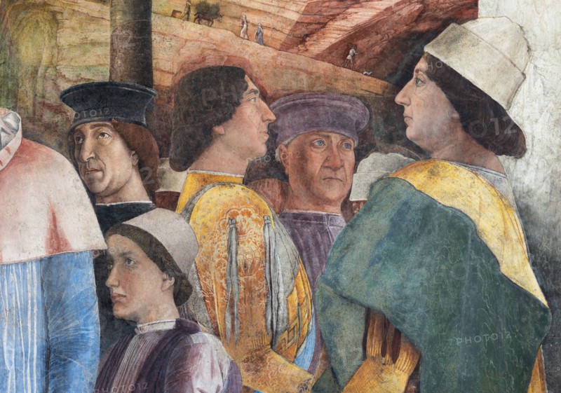 Ducal Palace: south-west wall of the “Bridal Chamber or Camera Picta", which is a room located in the north-east tower of the Castle of San Giorgio in Mantua. It is famous for the cycle of frescoes that covers its walls, a masterpiece by Andrea Mantegna, created between 1465 and 1474.
The wall, on the theme of “The Meeting” is divided into three sectors. In the one on the left the actual meeting takes place, in the central one some cherubs hold a dedicatory plaque and in the one on the right the marquis's court parades.
Detail of the right part of the wall: Federico Gonzaga is on the far right. The generous folds of his dress are a ploy to hide his kyphosis. Federico is in conversation with two characters, one in front and the other in the background, indicated by some as Christian I of Denmark
and Frederick III of Habsburg, figures who well represent the family's pride in royal kinship. Finally, the boy in the center is the last son of the marquis, the prothonotary Ludovico.
Palaz...