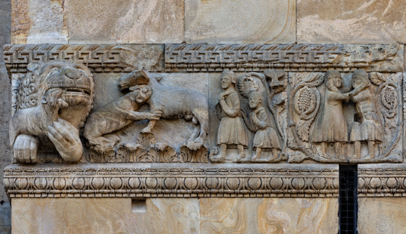 Fidenza, duomo (cattedrale di San Donnino), torre di destra (Torre del Trabucco), fronte ovest: particolare del fregio con “Storie di Berta, Milone e Rolandino” raccontate da due chanson de geste tra la fine del XII e l'inizio del XIII secolo. 
Da sinistra, un leoncino – allegoria di Rolandino – azzanna al collo un cavallo. Milone, seguito dal figlio Rolandino, va nel bosco per procurarsi legna da vendere. Milone lotta con un bandito che vorrebbe rapire Berta rimasta incinta.
Opera di Benedetto Antelami e bottega.


[ENG]
Fidenza, duomo (Cathedral of San Donnino), right tower (Trabucco Tower), west front: detail of the frieze with “Stories of Berta, Milone and Rolandino” told by two Chanson de Geste between the end of the 12th and the beginning of the 13th century.
From the left, a young lion – an allegory of Rolandino – bites a horse in the neck. Milone, followed by his son Rolandino, goes into the woods to get wood to sell. Milone fights with a bandit who wants to kidnap Berta...