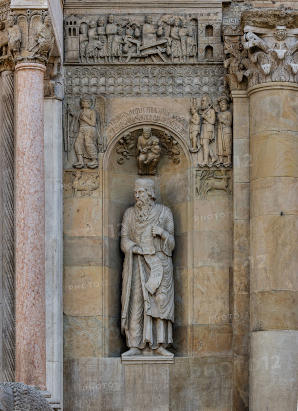 Fidenza, duomo (Cattedrale di San Donnino):
“Il Profeta Ezechiele” di Benedetto Antelami.
Il profeta sorregge un cartiglio che rimanda al significato della chiesa come "Porta del Cielo"; vi si legge: Ezechiel Propheta; vidi portam in domo Domini clausam (Ezechiele Profeta; ho visto chiusa la porta nella casa del Signore). 
Nella calotta della nicchia è posto un bassorilievo raffigurante una Madonna col Bambino circondata da racemi di fiori e di frutta sormontata da una scritta che ne spiega il significato teologico.
Ai lati della nicchia, sempre in simmetria con la parte sinistra della facciata, vediamo due formelle rappresentanti un'arpia e un centauro che colpisce un cervo, e, più in alto, la figura di un Angelo intento verosimilmente ad indicare ad una famiglia di pellegrini poveri la strada della Via Francigena.
Sopra una fascia ornata con motivi geometrici é il bassorilievo del “Miracolo della donna gravida”.

[ENG]
Fidenza, cathedral (Cathedral of San Donnino):
“The Prop...
