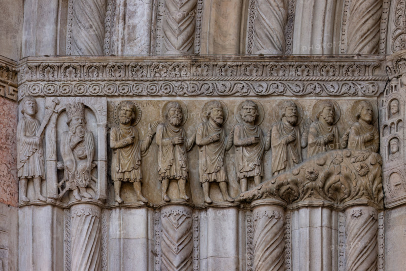Fidenza, duomo (Cattedrale di San Donnino), facciata, portale maggiore: dettaglio dell’archivolto con “Storie di San Donnino”.
L'imperatore Massimiano si accarezza la barba (meditando la vendetta). Il santo fugge assieme ai suoi compagni (Donnino è il primo da sinistra, con l'aureola abbellita da un cerchio di piccoli fori).
Opera di  Benedetto Antelami e bottega.

[ENG]
Fidenza, duomo (Cathedral of San Donnino), facade, main portal: detail of the archivolt with “Stories of St. Donnino”. Emperor Maximian strokes his beard (meditating revenge).
The saint flees with his companions (Donnino is the first from the left, with his halo embellished with a circle of small holes).
Work by Benedetto Antelami and workshop.
Cattedrale di San Donnino, Fidenza (PR), Emilia-Romagna, Italia - Italy