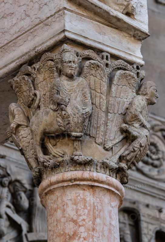 Fidenza, Duomo (Cattedrale di San Donnino), facciata, portale maggiore, protiro: il capitello di destra con “i Quattro Evangelisti”. Al centro “S. Marco”, che reca, incisa sul cartiglio l’iscrizione a lettere capitali: V[O] / X / CLA / MANTIS (Vox Clamantis (Mc 1,3) = Voce di chi chiama…). 
Opera di Benedetto Antelami e bottega.

[ENG]
Fidenza, Duomo (Cathedral of San Donnino), facade, main portal, prothyrum:  the right capital with “the Four Evangelists”. In the centre "St. Mark”, which bears, engraved on the cartouche, the inscription in capital letters: V[O] / X / CLA / MANTIS (Vox Clamantis (Mc 1,3) = Voice of one who calls…)
Work by Benedetto Antelami and workshop.
Cattedrale di San Donnino, Fidenza (PR), Emilia-Romagna, Italia - Italy