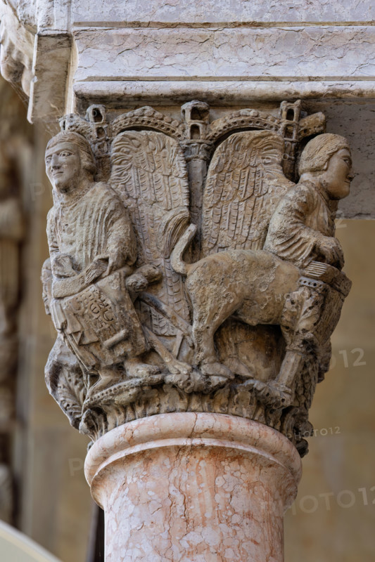 Fidenza, Duomo (Cattedrale di San Donnino), facciata, portale maggiore, protiro: il capitello di destra con “i Quattro Evangelisti”.  A sinistra “S. Matteo”  con piedi umani che porta l’iscrizione: LIBER. / [G]ENE / [R]ACI / [ON]NIS. (Liber generationis (Mt 1,1)= Libro della generazione…)
Opera di Benedetto Antelami e bottega.

[ENG]
Fidenza, Duomo (Cathedral of San Donnino), facade, main portal, prothyrum:  the right capital with “the Four Evangelists”. On the left “St. Matthew” with human feet bearing the inscription: LIBER. / [G]ENE / [R]ACI / [ON]NIS. (Liber generationis (Mt 1,1) = Book of the generation…).
Work by Benedetto Antelami and workshop.
Cattedrale di San Donnino, Fidenza (PR), Emilia-Romagna, Italia - Italy