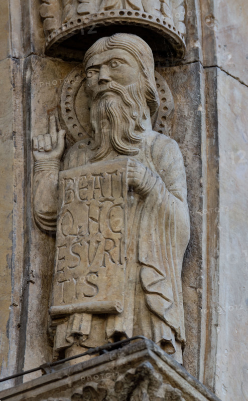 Fidenza, Duomo (Cathedral of San Donnino), facade, main portal: detail of the archivolt with “Allegories of the Beatitudes”. An apostle with the inscription: BEATI / Q[VI] N[VN]C / ESVRI/TIS = Blessed are those who hunger (Lc 6, 21). 
Work by Benedetto Antelami and workshop.
Cattedrale di San Donnino, Fidenza (PR), Emilia-Romagna, Italia - Italy