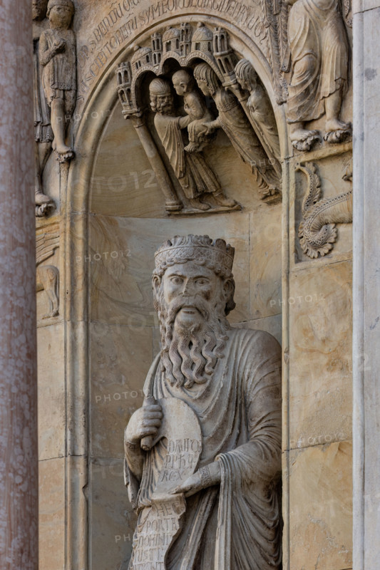 Fidenza, duomo (Cattedrale di San Donnino), sculture tra il portale maggiore e quello di sinistra: la nicchia con il “Re David” di Benedetto Antelami.
Il profeta sorregge un cartiglio sul quale si legge la seguente iscrizione a lettere capitali: DAUID / PPHA / REX / HEC / PORTA / DOMINI / IUSTI: / INTRANT PEREAM (David Propheta Rex – Hec porta Domini iusti intrant per eam [Salmo 118 (117),20]).
Lo sguardo di Re David è rivolto a chi entra nella cattedrale dal portale maggiore.

[ENG]
Fidenza, duomo (Cathedral of San Donnino), sculptures between the main portal and the left one: the niche with “King David” by Benedetto Antelami.
The prophet holds a scroll on which the following inscription can be read in capital letters: DAUID / PPHA / REX / HEC / PORTA / DOMINI / IUSTI: / INTRANT PEREAM (David Propheta Rex – Hec porta Domini iusti intrant per eam [Psalm 118 (117),20]).
King David's gaze is directed at those entering the cathedral from the main portal.
Cattedrale di San Donnino,...