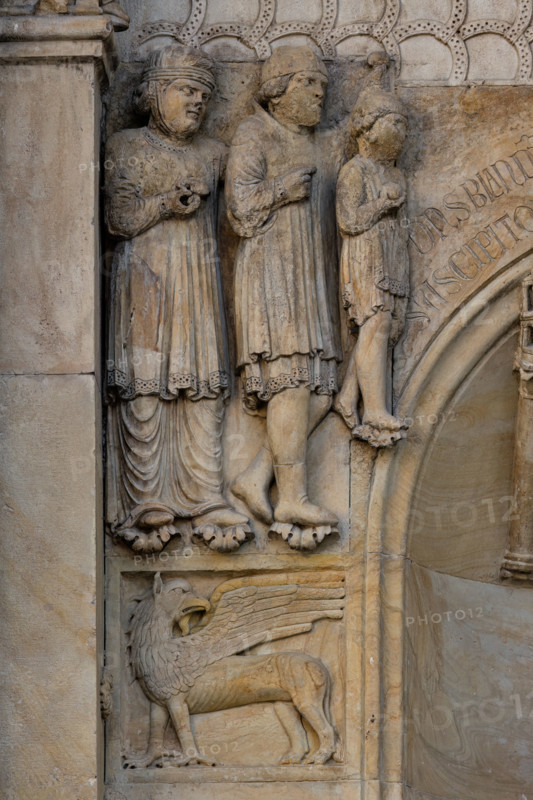 Fidenza, duomo (Cattedrale di San Donnino), sculture tra il portale maggiore e quello di sinistra vicino alla nicchia con il “Re David” di Benedetto Antelami.
Particolare con le figura di un grifo sormontata dal bassorilievo raffigurante verosimilmente una famiglia di pellegrini ricchi in viaggio per Roma. 

[ENG]
Fidenza, cathedral (Cathedral of San Donnino), sculptures between the main portal and the left one near the niche with the “King David” by Benedetto Antelami.
Detail with the figure of a griffin surmounted by the bas-relief probably depicting a family of rich pilgrims traveling to Rome.
Cattedrale di San Donnino, Fidenza (PR), Emilia-Romagna, Italia - Italy