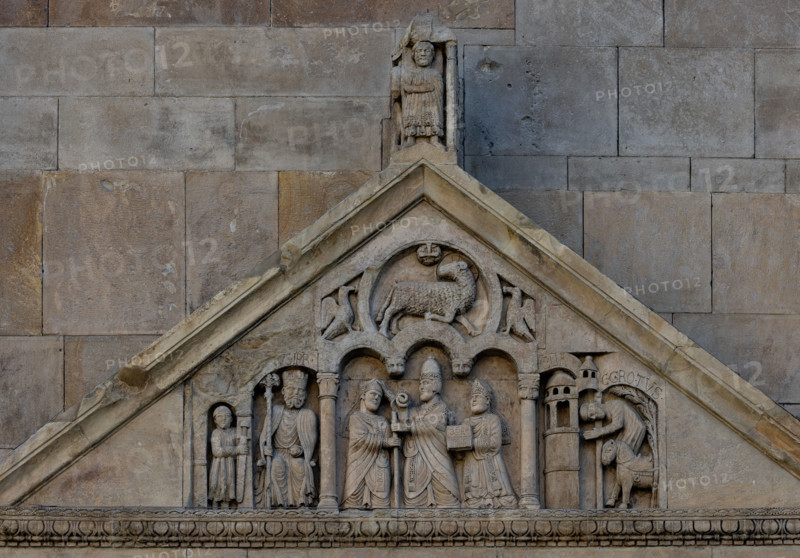 Fidenza, duomo (Cattedrale di San Donnino), portale sinistro, timpano. Nel frontone si leggono, da sinistra, tre scene: L'imperatore Carlo Magno, con un armigero alla sua destra;
Papa Adriano II che porge all'arciprete di San Donnino la mitria e il pastorale (simboli della dignità episcopale); il miracolo dell'ammalato guarito (miracolo compiuto da San Donnino).
Nell’acroterio sul timpano, é raffigurato un personaggio, probabilmente Oberto II Pallavicino condottiero posto da Federico II di Svevia alla guida della città dal 1249 al 1268.

Opera di Benedetto Antelami e bottega.

[ENG]
Fidenza, duomo (Cathedral of San Donnino), left portal, tympanum. In the pediment, from the left, three scenes can be read: Emperor Charlemagne, with a man-at-arms to his right;
Pope Adrian II who offers the archpriest of San Donnino the mitre and the pastoral staff (symbols of episcopal dignity); the miracle of the healed sick man (miracle performed by San Donnino).
In the acroterion on the tympan...