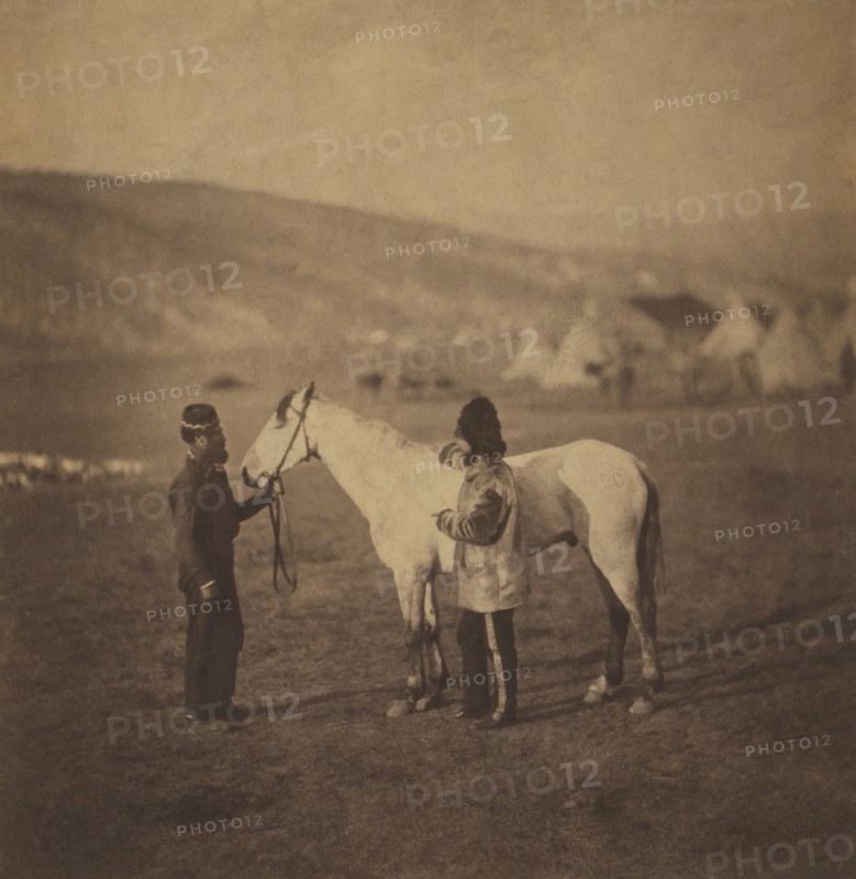 British Colonel George Clarke, Royal Scots Greys, Full-length Portrait, wearing uniform, Standing beside his Wounded Horse, Sultan and another Man with Encampment of Tents in Background, Crimean War, Crimea, Ukraine, by Roger Fenton, 1855