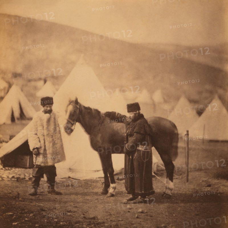 British Colonel Alexander Low, 4th Light Dragoons, Full-Length Standing Portrait in Winter Uniform with Servant and Horse, Military Tents in Background, Crimean War, Crimea, Ukraine, by Roger Fenton, 1855