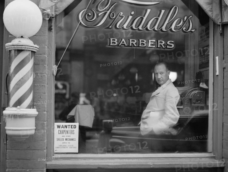 Portrait of Barber in Barber Shop Window, Help Wanted Sign Looking for Skilled Labor Resources Posted in Window by Virginia State Employment Service, Friddle's Barbers, Harrisonburg, Virginia, USA, John Vachon for Office for Emergency Management, May 1941