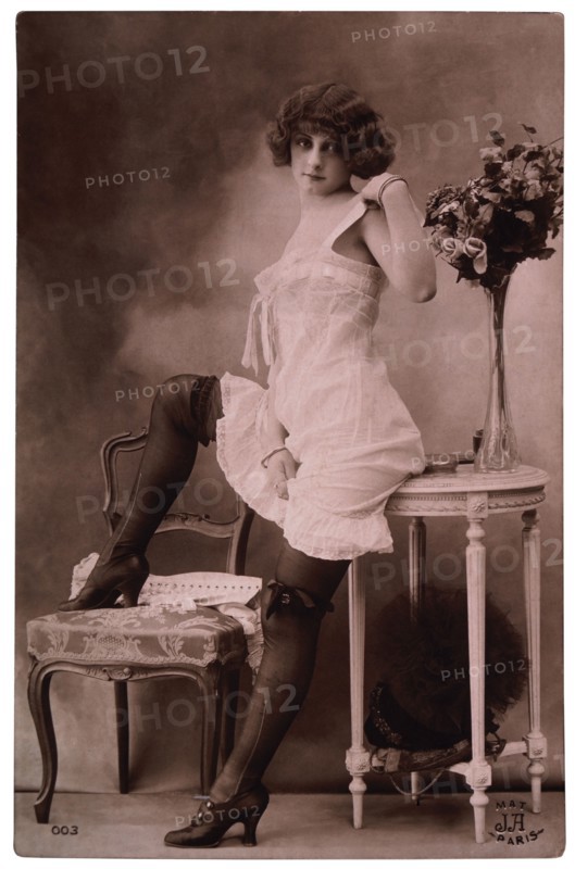 French Lingerie Model Leaning on Table With One Leg Raised on Chair, 1920