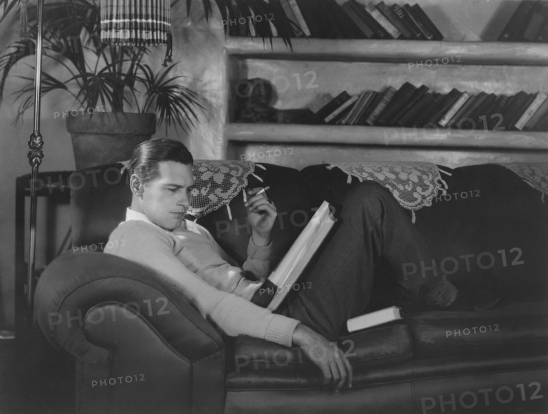 Actor Richard Arlen, Publicity Portrait Smoking Cigarette and Reading Script on Sofa, 1930's