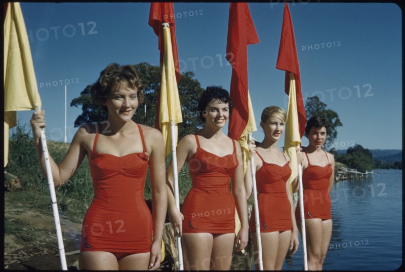 Four Young Adult Women Wearing Red One-Piece Bathing Suits and Holding Red and Yellow Flags, Australia, 1960