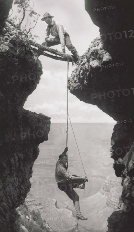 Photographer, Emery or Elsworth Kolb, Suspended on Climber's Rope in Crevasse and Photographing Canyon Wall as Another Man Straddles Cliff Opening while Holding the Rope, Grand Canyon, Arizona, USA, by Kolb Brothers, 1908