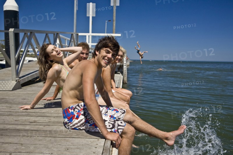 Two Smiling Young Couples Sitting on Edge of Pier