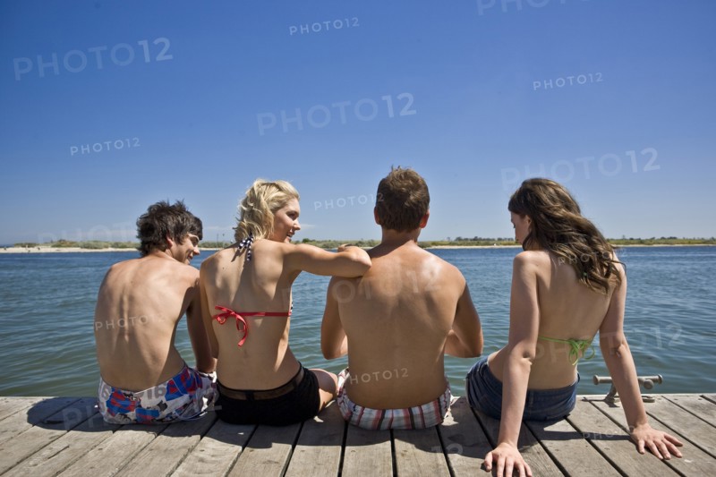 Two Young Couples Sitting on Edge of Pier, Rear View