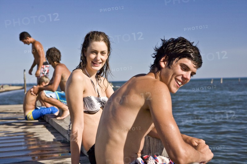 Smiling Young Couple Sitting on Edge of Pier
