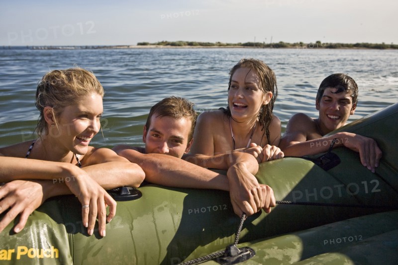 Two Smiling Young Couples in Water Resting on Side of Dinghy