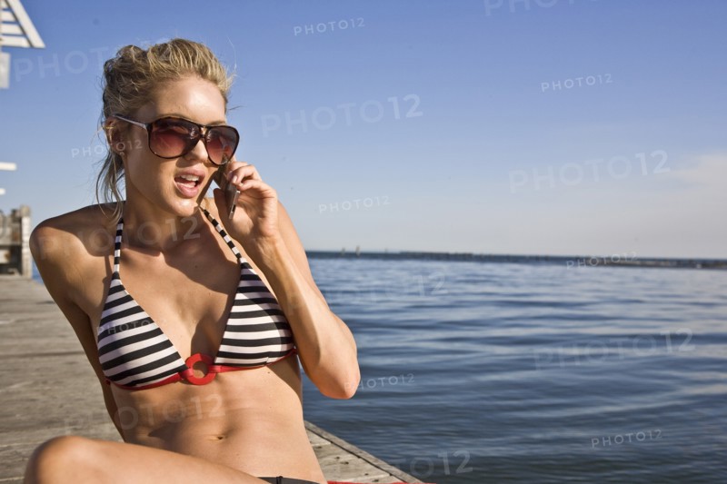 Young Woman Sunbathing and Talking on Cell Phone on Pier