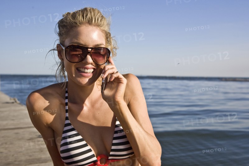 Smiling Young Woman Sunbathing and Talking on Cell Phone on Pier