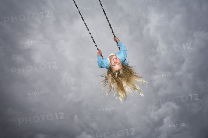 Girl On Swing against Grey Cloudy Sky