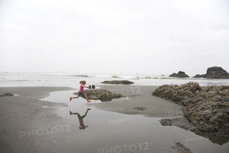 Girl Jumping Over Tidal Pool on Beach