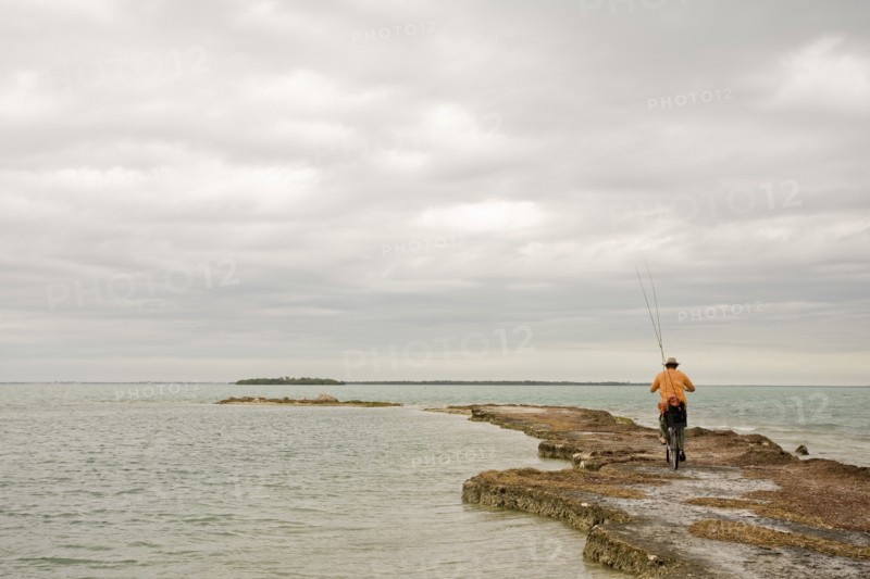 Man Riding Bicycle With Fishing Rods on Beach, Florida Keys, USA