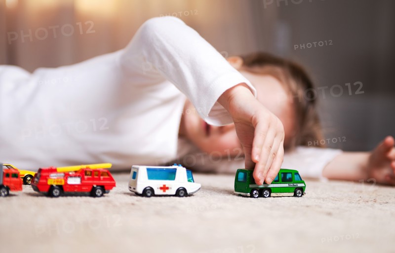 Young Girl Laying on Floor and Playing with Toy Cars and Trucks