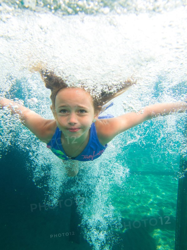 Young Girl Swimming Underwater in Pool Surrounded by Bubbles