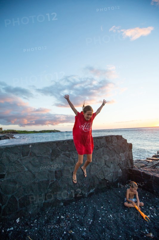 Young Girl Jumping off Lava Rock Wall while her Brother is Playing in  Black Sand at Ocean Beach, Hawaii, USA