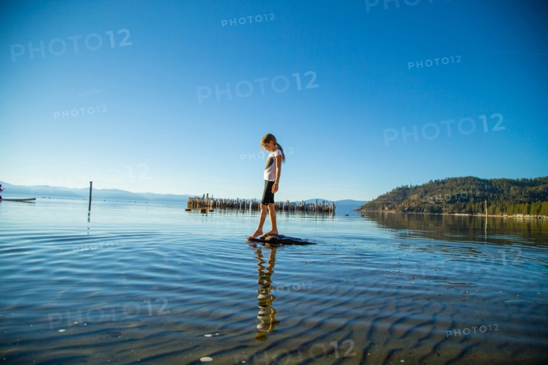Young Girl Standing on Rock Dipping her Toes into Shallow Water, Lake Tahoe, Nevada, USA