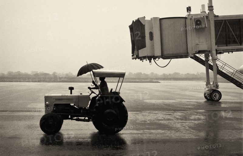 Man on Tractor Holding Umbrella at Airport