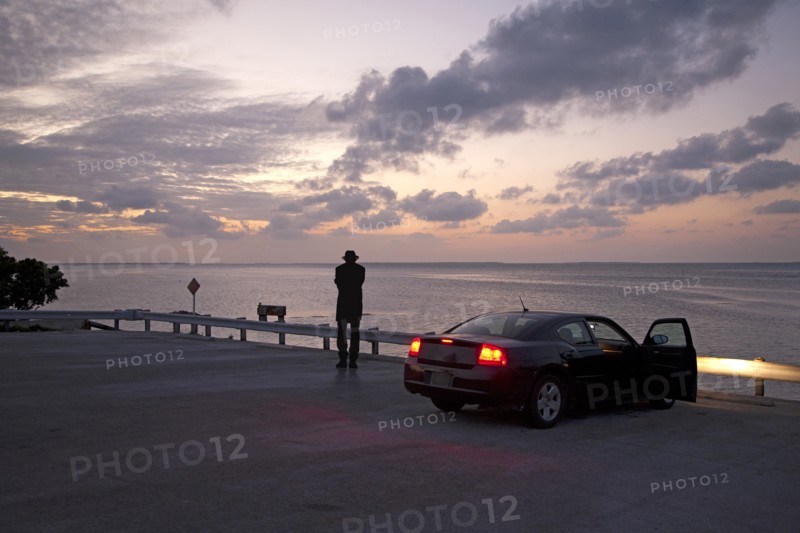 Rear View of Man near Parked Car Looking out to Sea at Sunset