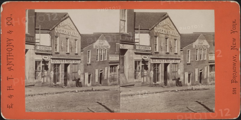 Man with Rifle sitting outside Commercial Building used as Slave Market