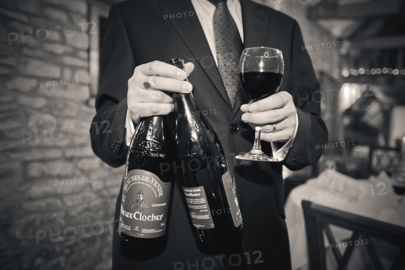 Man holding Wine Glass and Two Bottles of Red Wine at Wedding