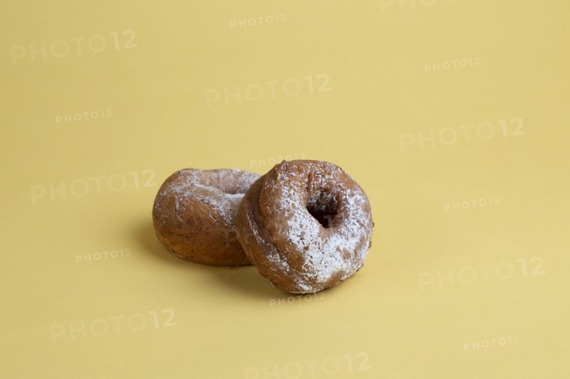 Two Doughnuts with Powdered Sugar on Yellow Background