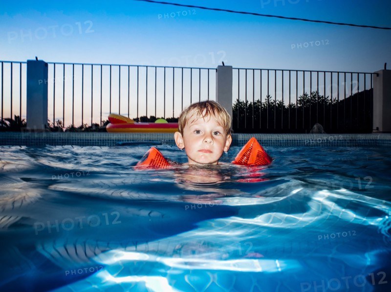 Young Boy floating in Swimming Pool at Sunset,