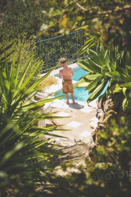 Rear View of Young Shirtless Boy standing near Swimming Pool,