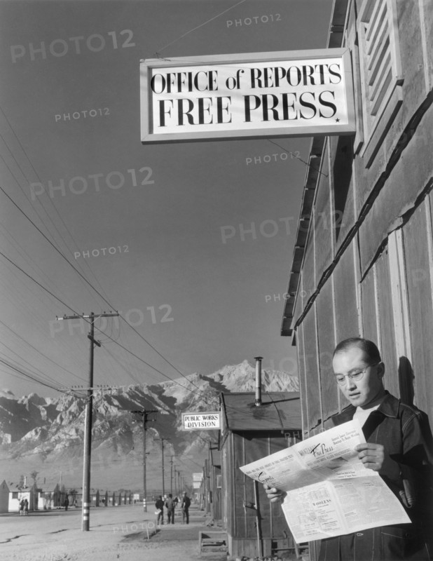 Editor Roy Takeno reading Copy of Manzanar Free Press in front of Newspaper Office