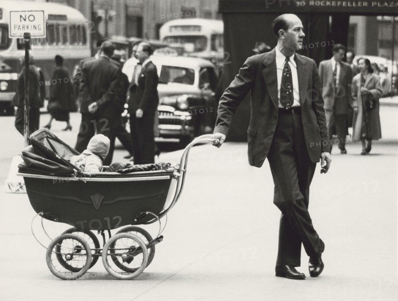 Man standing on Sidewalk with one hand on baby carriage
