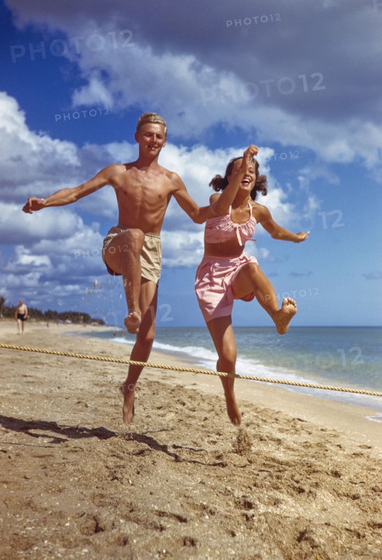 Young Adult Man and Young Adult Woman jumping over Rope on Sandy Beach