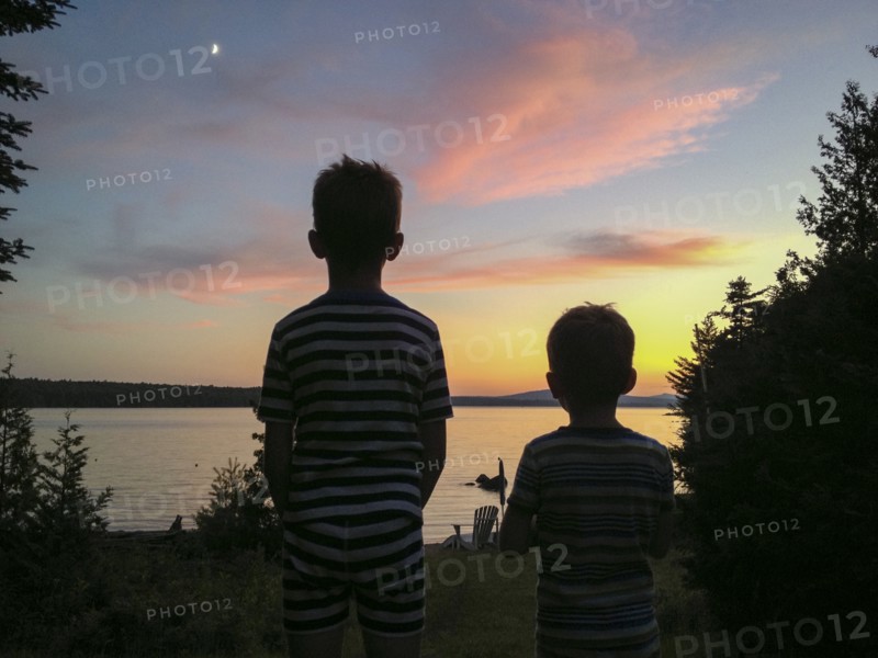 Rear view of two young boys viewing sunset at lake