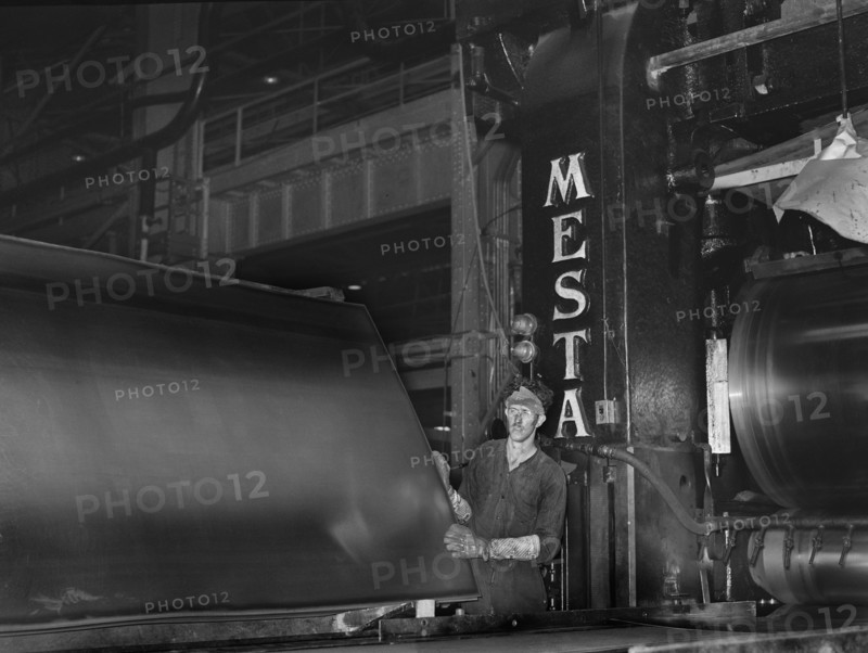 Steel worker examining sheet of steel after rolling