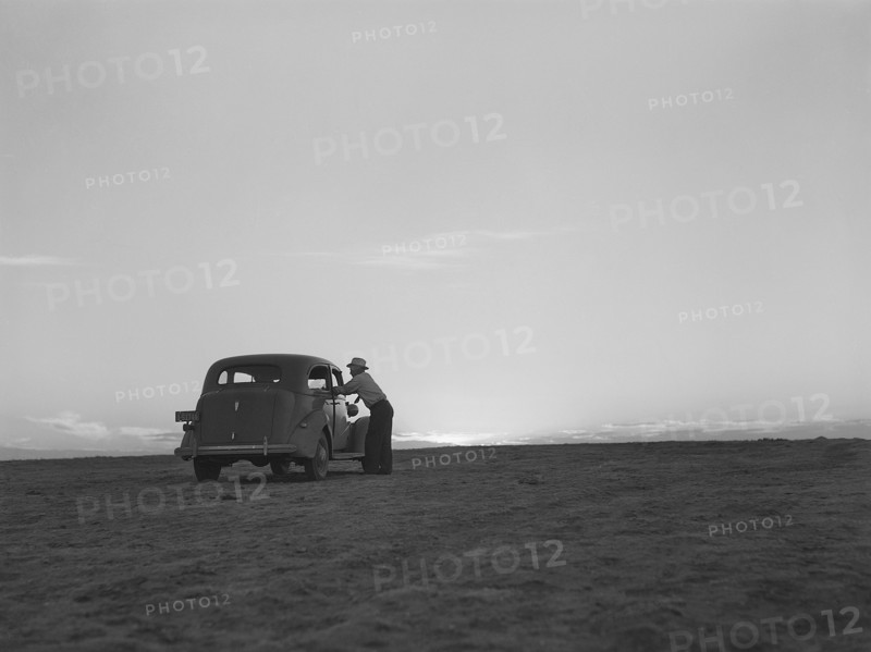 Man standing at car window talking to driver on the plain at sunset