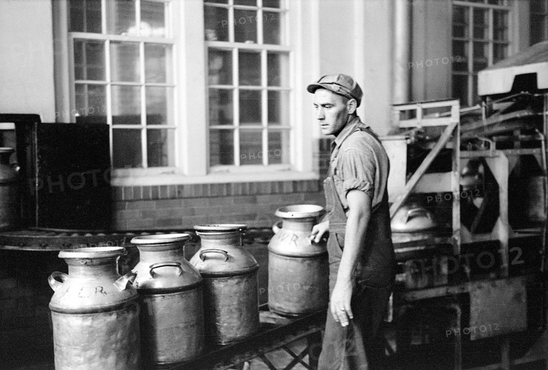 Worker running milk cans through sterilizing machine
