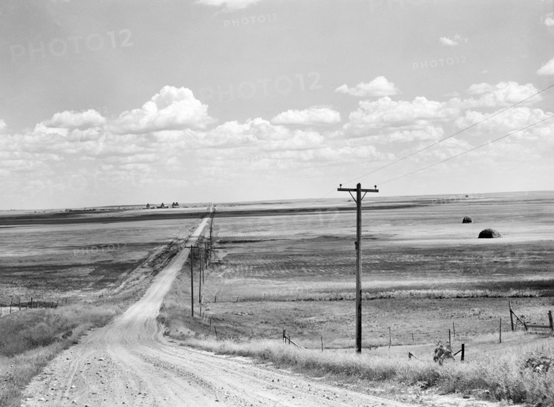 Dirt road through rural landscape with grain elevators in background, Homestead, Montana, USA, Marion Post Wolcott, U.S. Farm Security Administration, August 1941