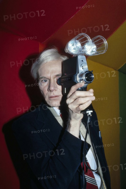 American pop artist Andy Warhol, half-length portrait looking through lens of Polaroid Polavision camera, Bernard Gotfryd, 1977
