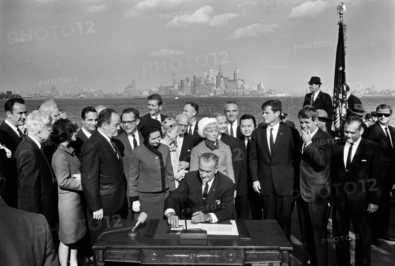 U.S. President Lyndon B. Johnson signing the Immigration and Nationality Act of 1965 as U.S. Vice President Hubert Humphrey, Lady Bird Johnson, Muriel Humphrey, Senator Edward Kennedy Senator Robert Kennedy, and others look on, Liberty Island, New York City, New York, USA, Yoichi Okamoto, October 3, 1965