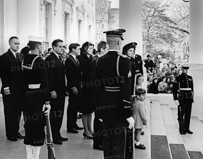 Former U.S. First Lady Jacqueline Kennedy stands with her children, Caroline Kennedy and John F. Kennedy, Jr., in the North Portico, prior to the funeral procession of President John Kennedy, standing behind Mrs. Kennedy: Attorney General, Robert Kennedy; Patricia Kennedy Lawford, R. Sargent Shriver, U.S. President Lyndon Johnson, members of the honor guard stand at attention; mourners and members of the press observe, White House, Washington, D.C., USA, Abbie Rowe, White House Photographs, November 24, 1963