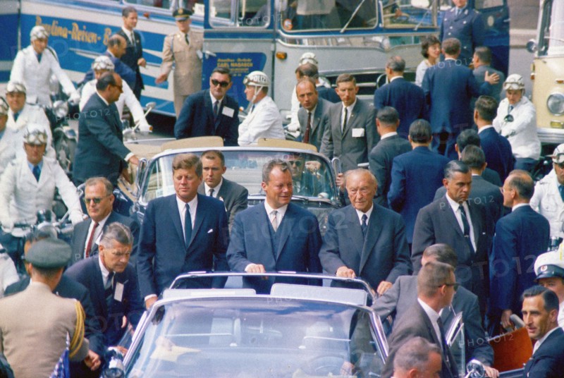 U.S. President John F. Kennedy standing with West Berlin Mayor Willy Brandt and West German Chancellor Konrad Adenauer in open convertible car during his motorcade through West Berlin, West Germany, Cecil Stoughton, White House Photographs, June 26, 1963